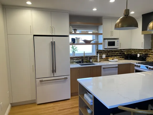 Finished kitchen with full-height white panelled cabinets around the fridge, open wood shelves over the sink and a navy island